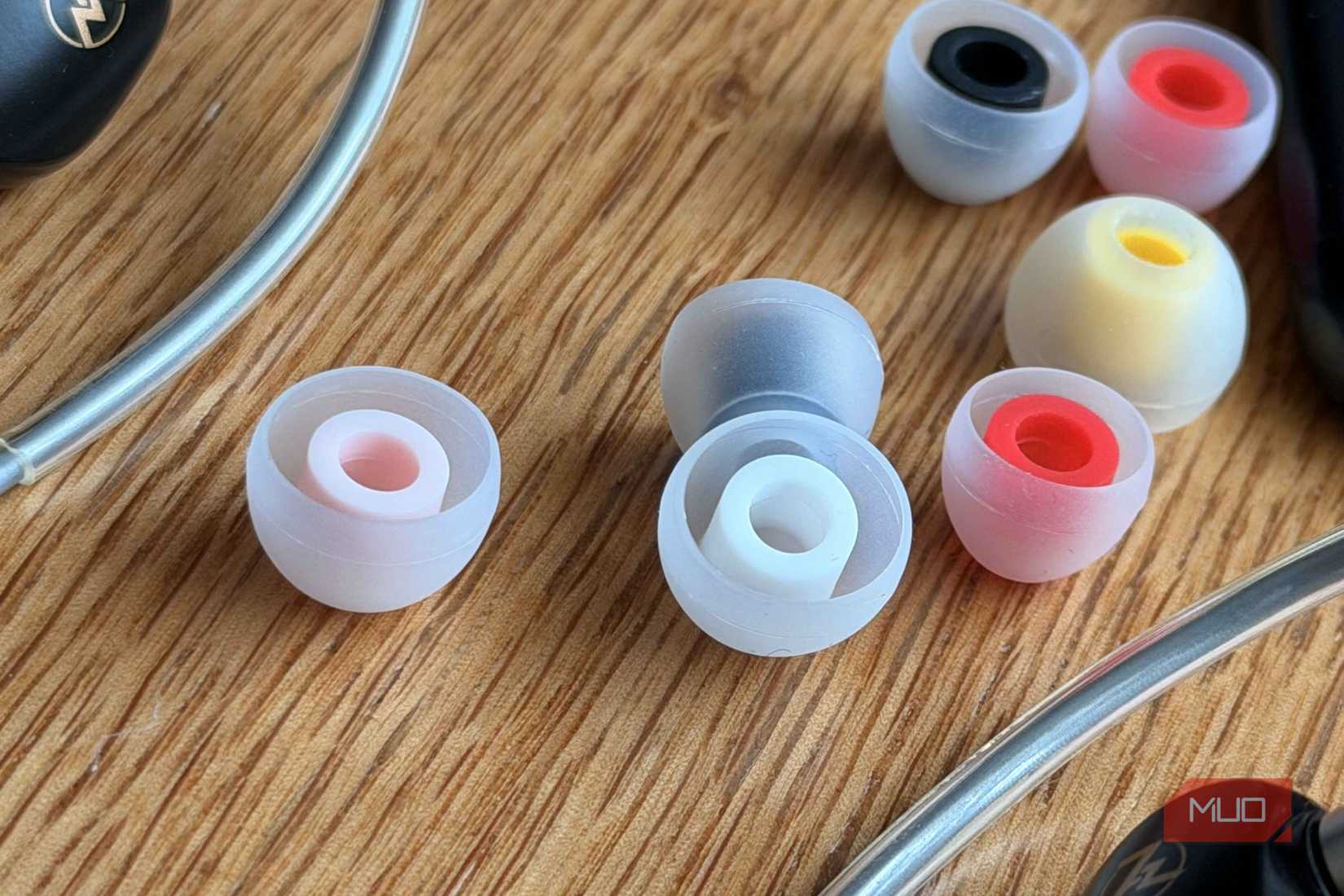 Close up of three silicone double flange ear tips in pink gray and red on a wooden surface with more tips blurred in the background