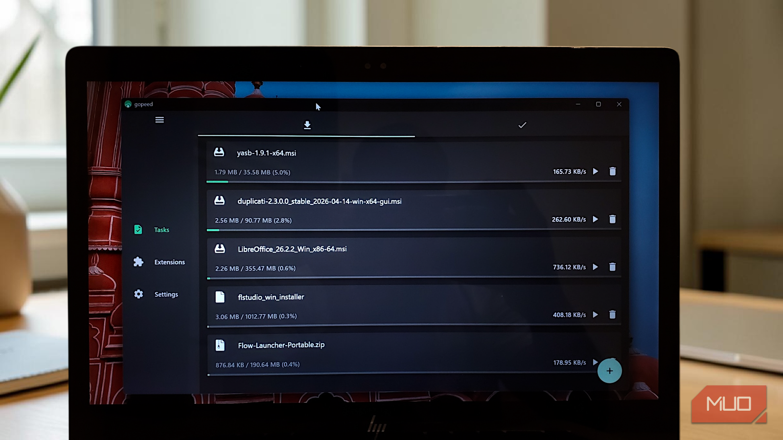 Laptop screen displaying active downloads in the Gopeed download manager.