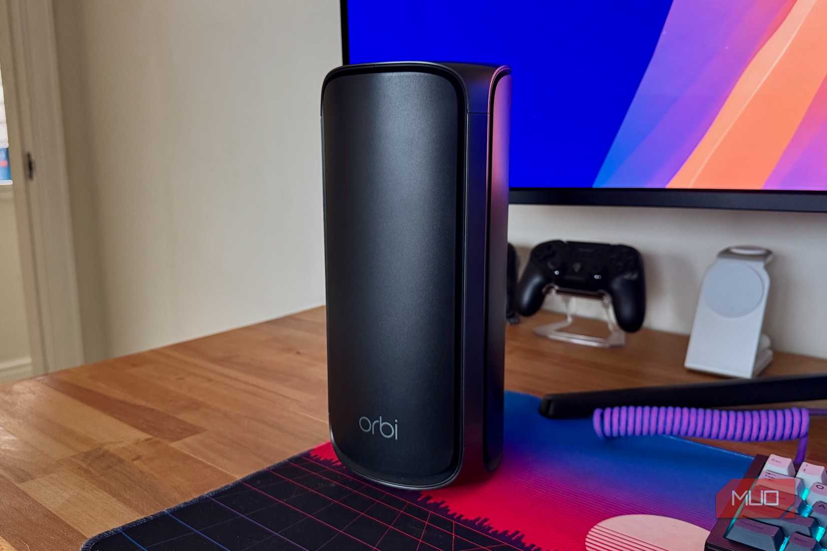 A Netgear Orbi router in black on a wooden desk
