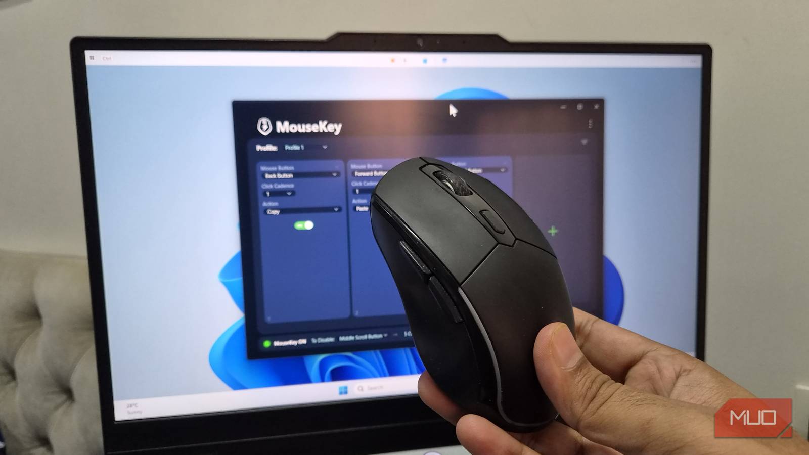 A hand holding a mouse with laptop in background showing MouseKey app