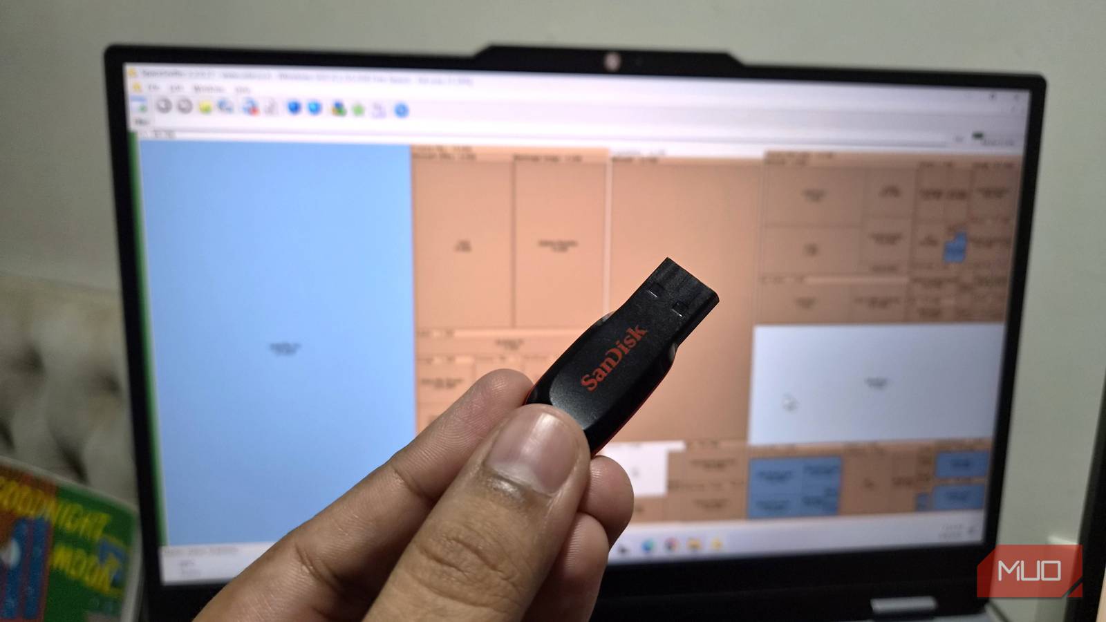 A hand holding a USB stick in front of a laptop