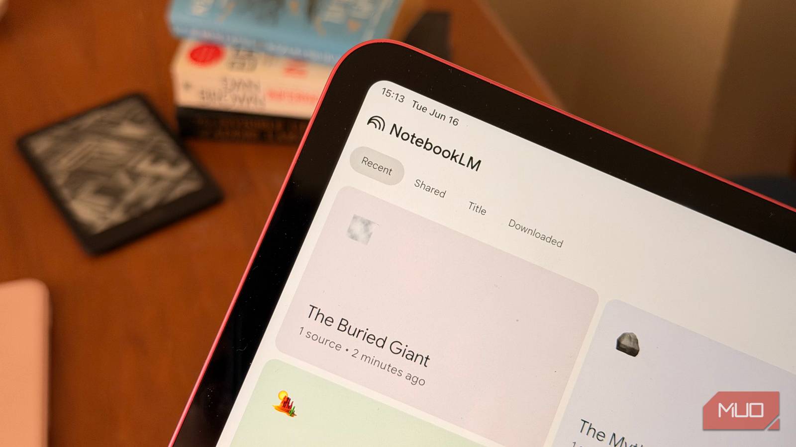 An iPad showing NotebookLM with books and a Kindle in the background
