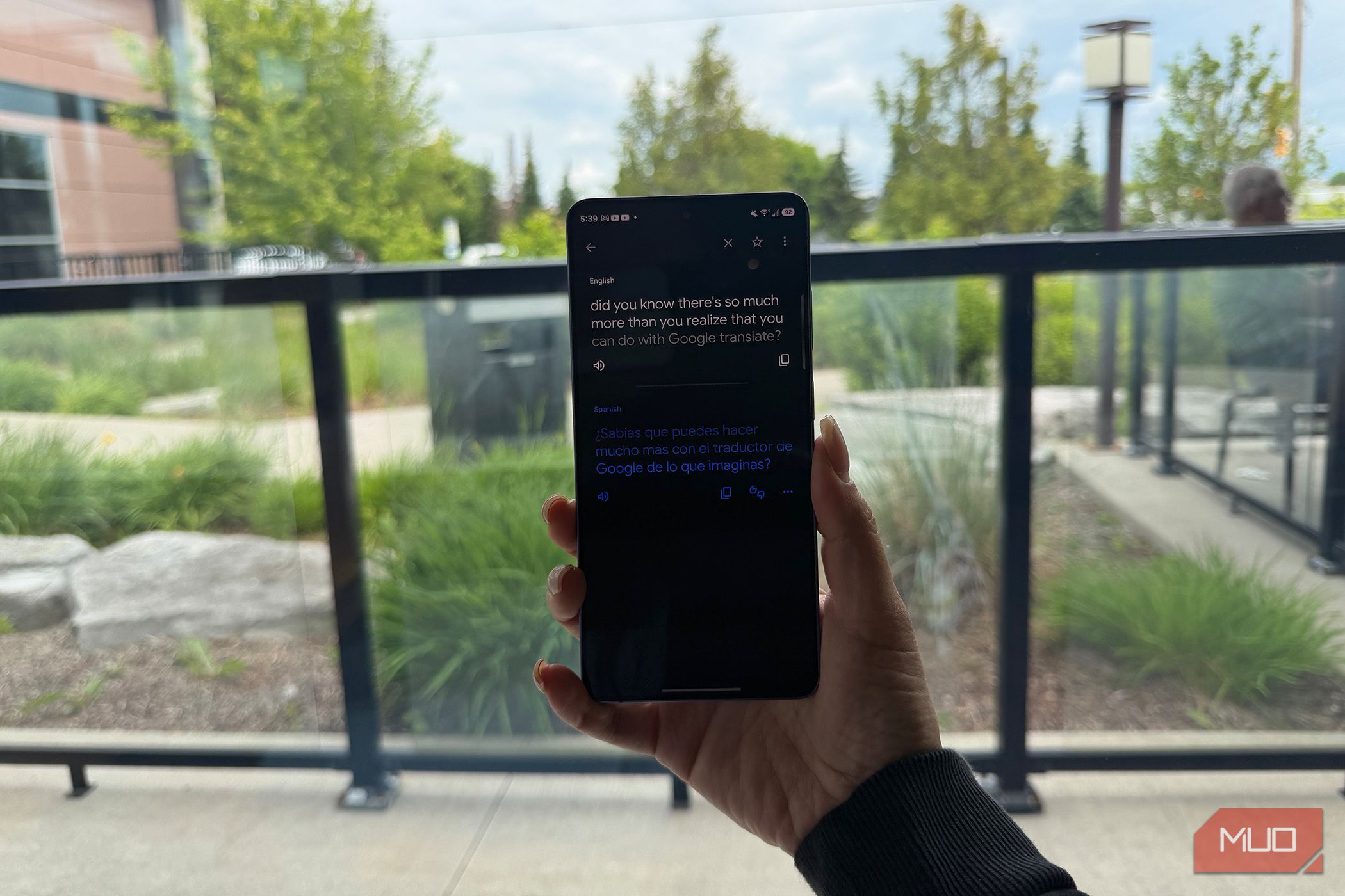 A hand holding a phone by a window showing Google Translate.