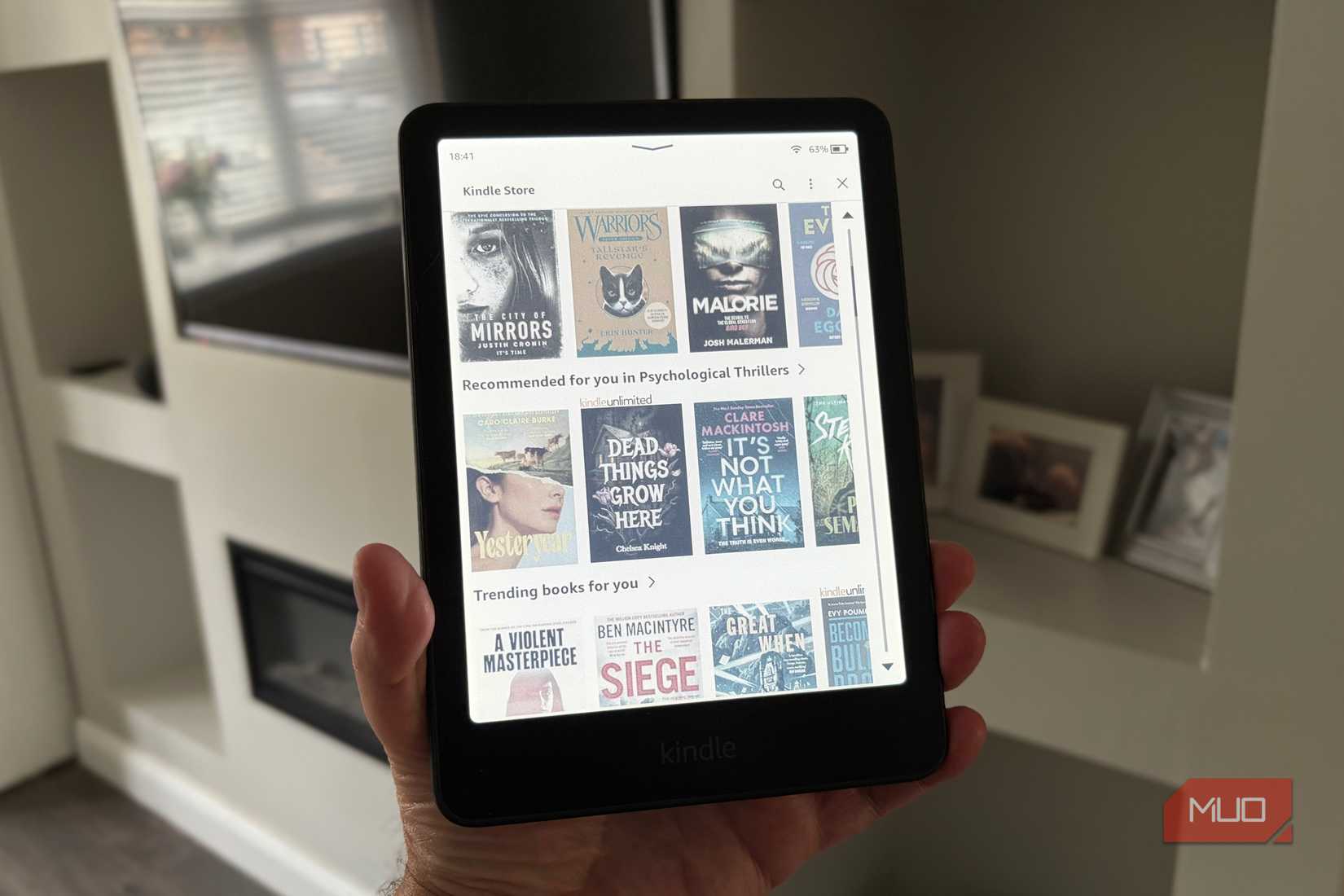 A Kindle Colorsoft held in-hand displaying a library of e-books