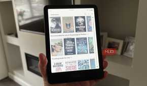 A Kindle Colorsoft held in-hand displaying a library of e-books