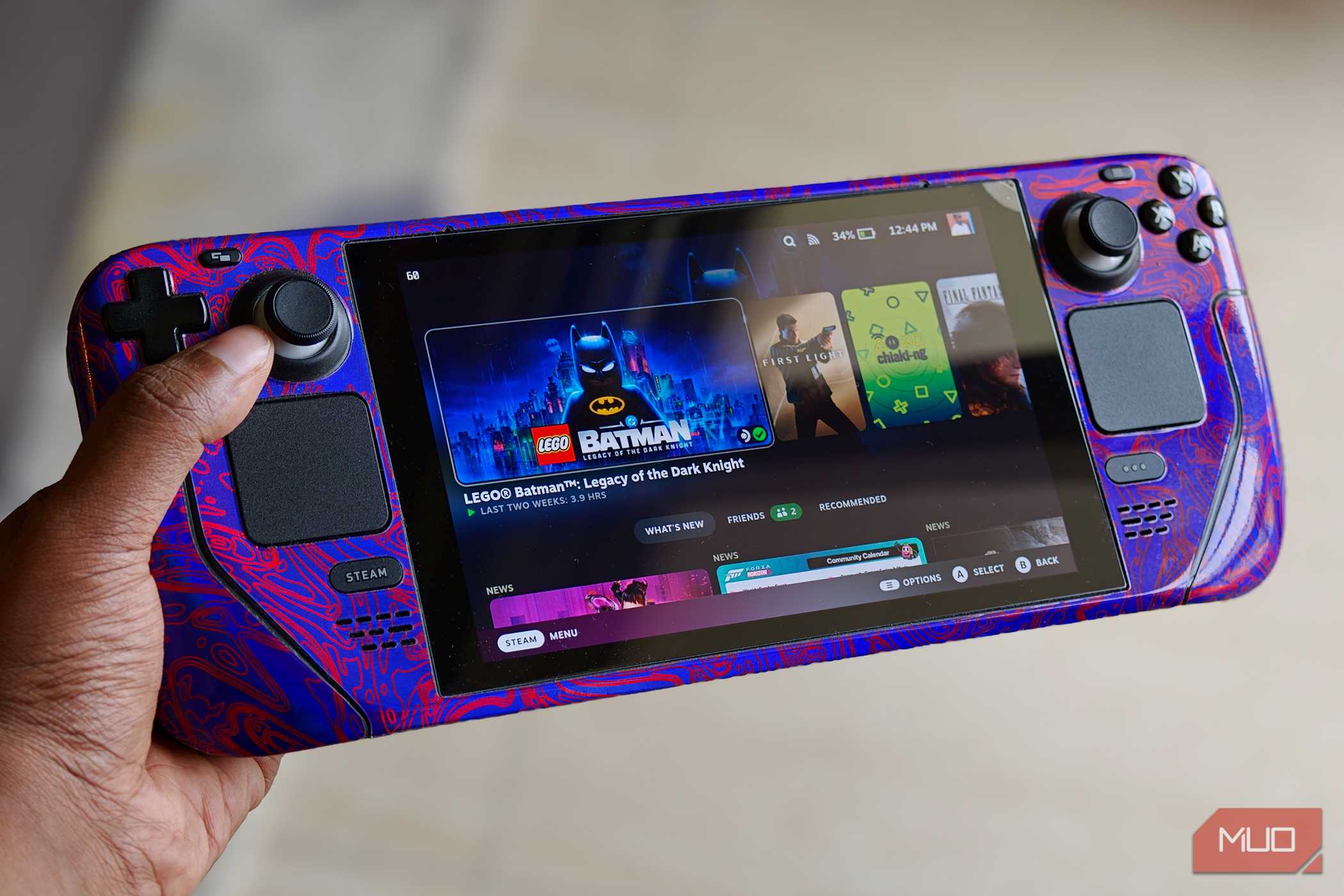 Hand holding a Steam Deck console showing LEGO Batman in Steam