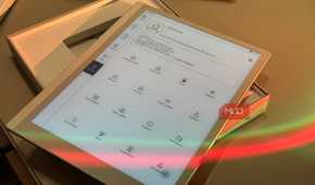 tablet device displaying app menu with various icons and options in wooden holder with colored light reflection