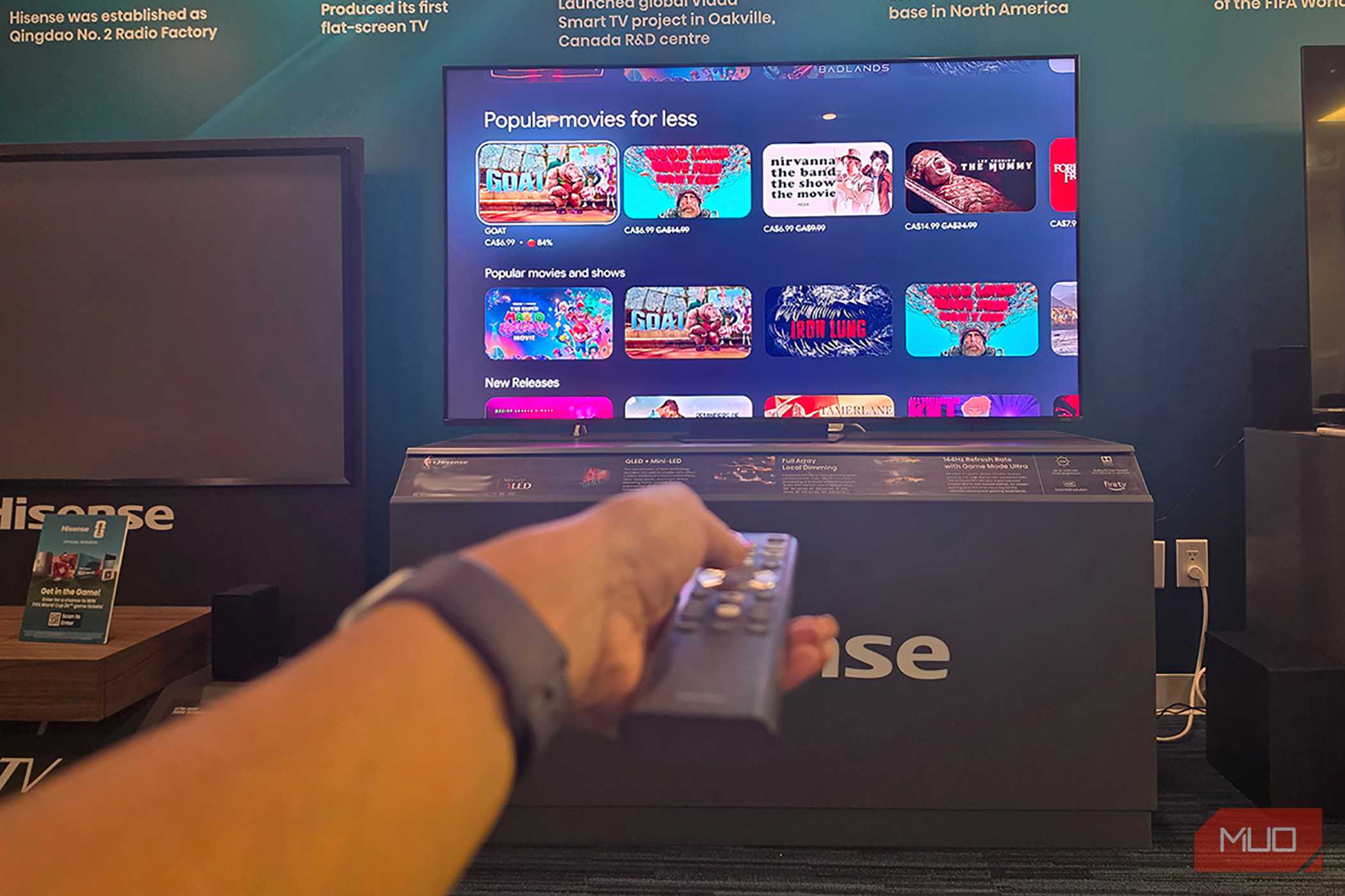 A hand holding a remote in front of a Hisense miniLED TV