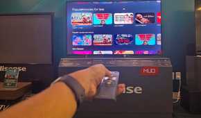 A hand holding a remote in front of a Hisense miniLED TV