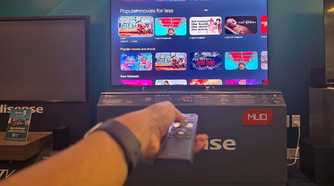 A hand holding a remote in front of a Hisense miniLED TV