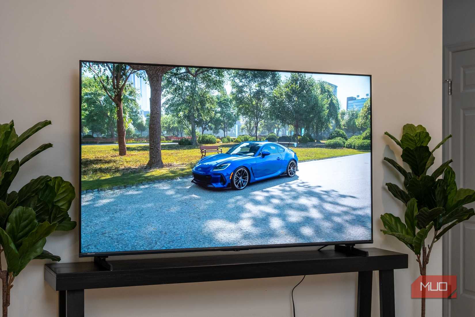 Hisense U6 on dark console table displaying a blue sports car parked in a tree-lined park in a video game.