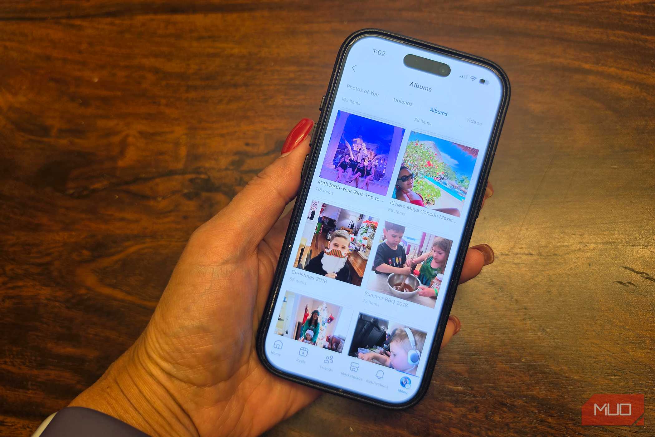 A hand holding an iPhone showing a Facebook photo album.