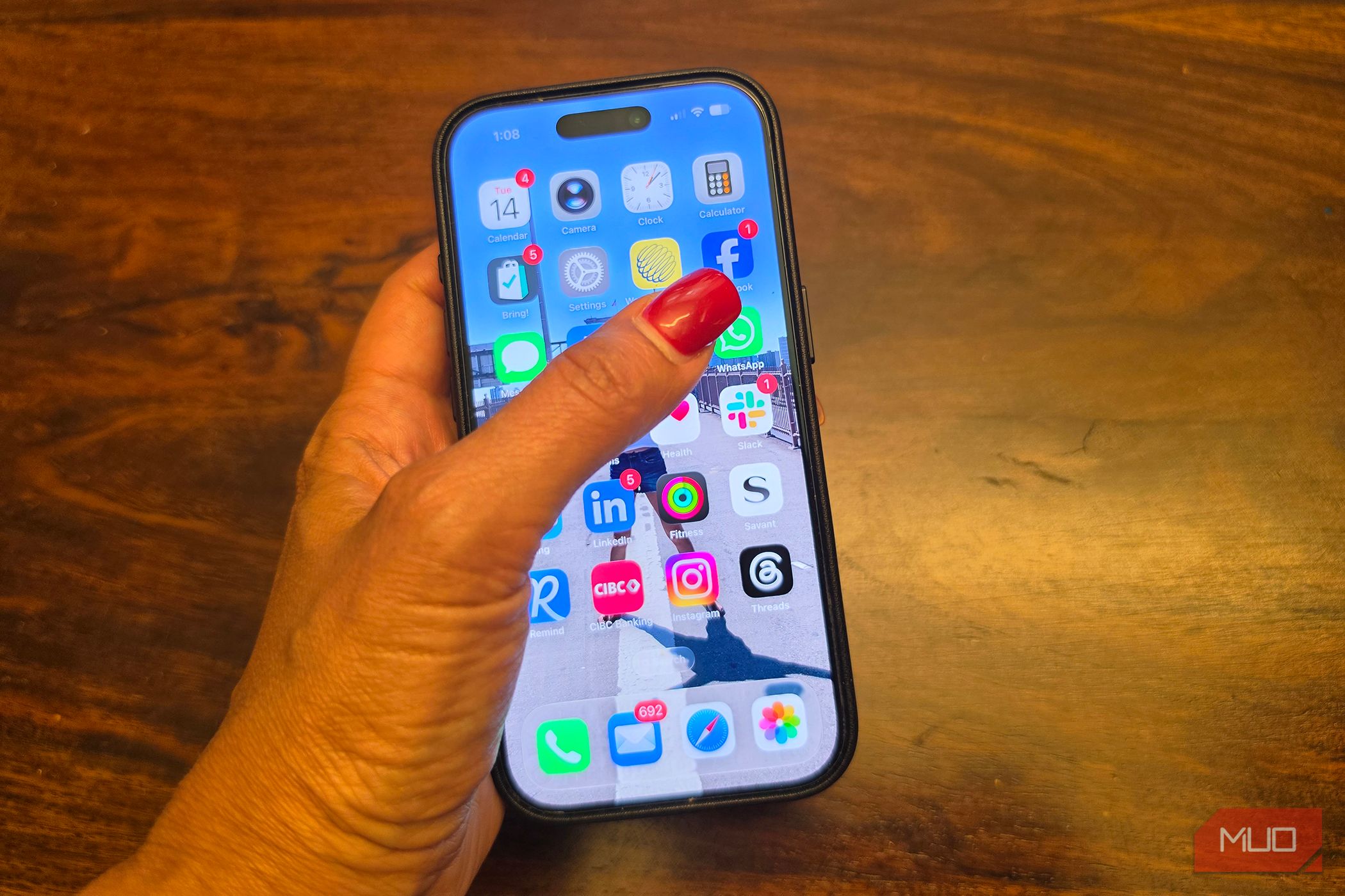 A hand holding an iPhone with a finger pointing to the Facebook app.