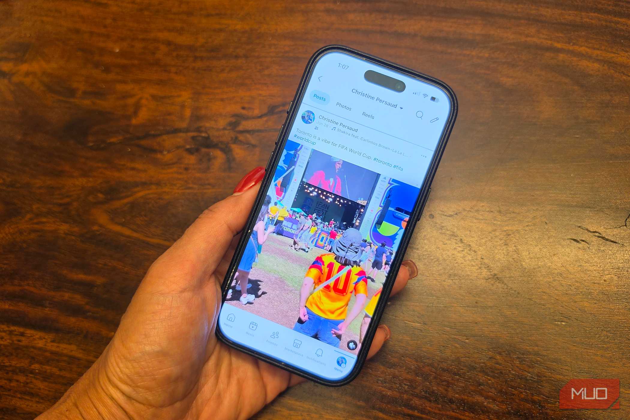 A hand holding an iPhone showing a Facebook Feed.