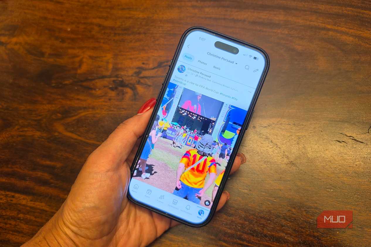 A hand holding an iPhone showing a Facebook Feed.