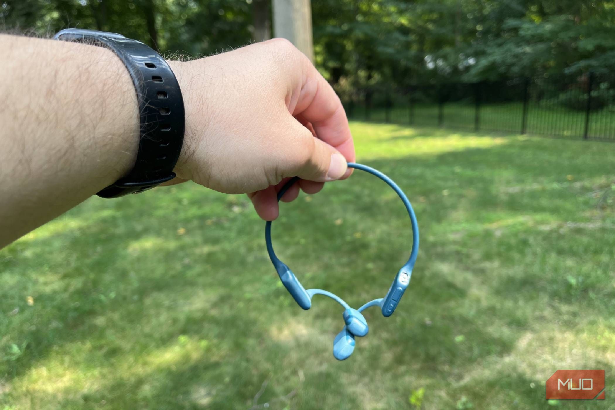 A pair of Shokz OpenRun Pro bone conduction headphones being held in a yard.