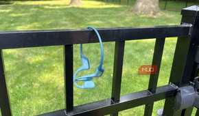 Shokz OpenRun Pro bone conduction headphones hanging on a gate.