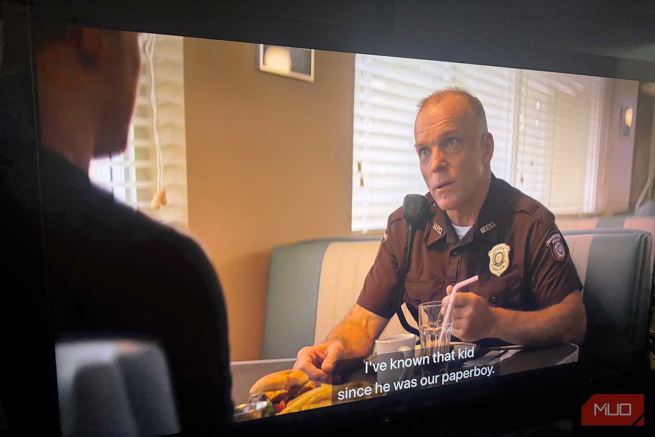 Side view of a TV playing an episode of Reacher with captions as a man talks in a diner.