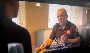 Side view of a TV playing an episode of Reacher with captions as a man talks in a diner.