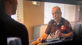 Side view of a TV playing an episode of Reacher with captions as a man talks in a diner.