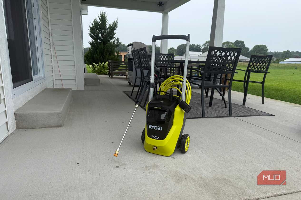 Ryobi pressure washer with spray wand on covered concrete patio with dining table and field in background
