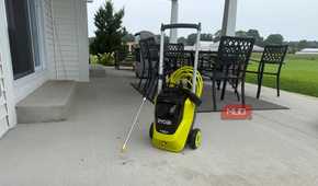 Ryobi pressure washer with spray wand on covered concrete patio with dining table and field in background