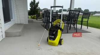 Ryobi pressure washer with spray wand on covered concrete patio with dining table and field in background