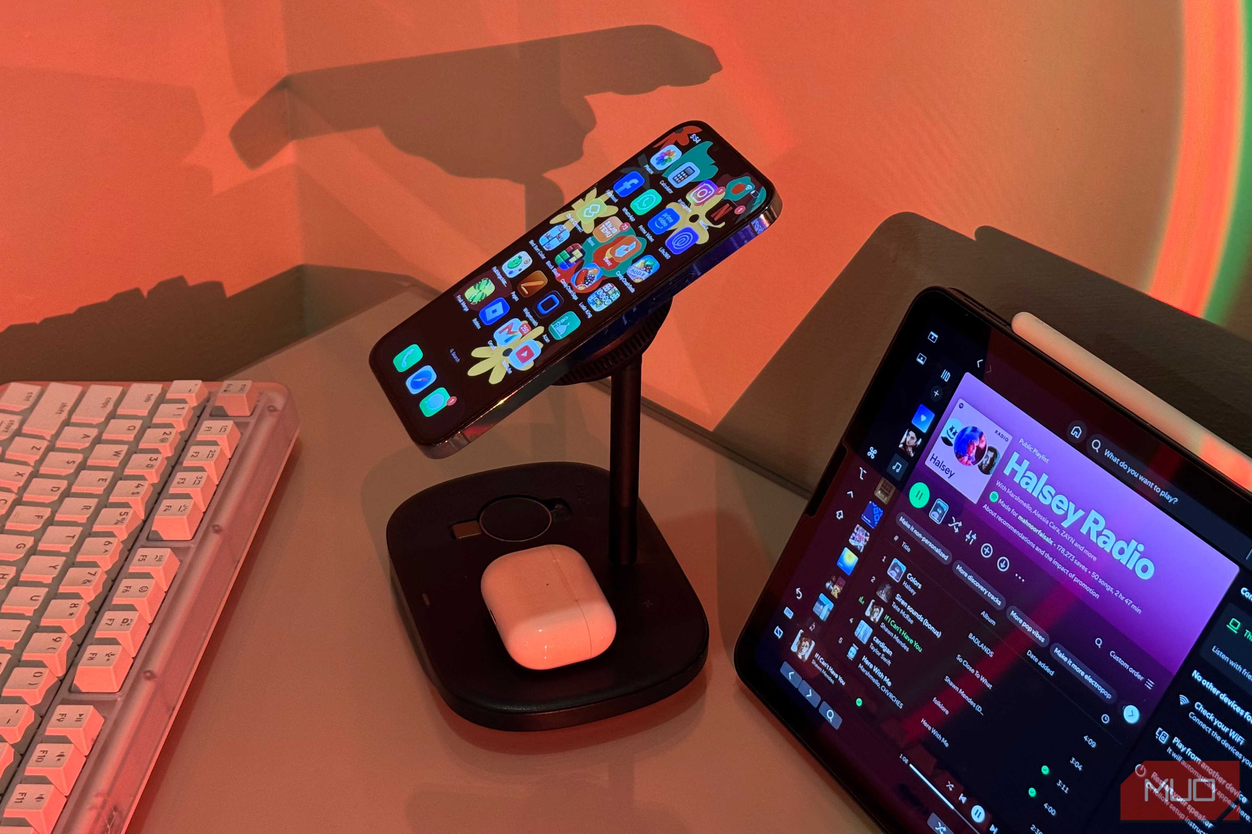 iPhone tilted on Baseus stand with AirPods and iPad Spotify