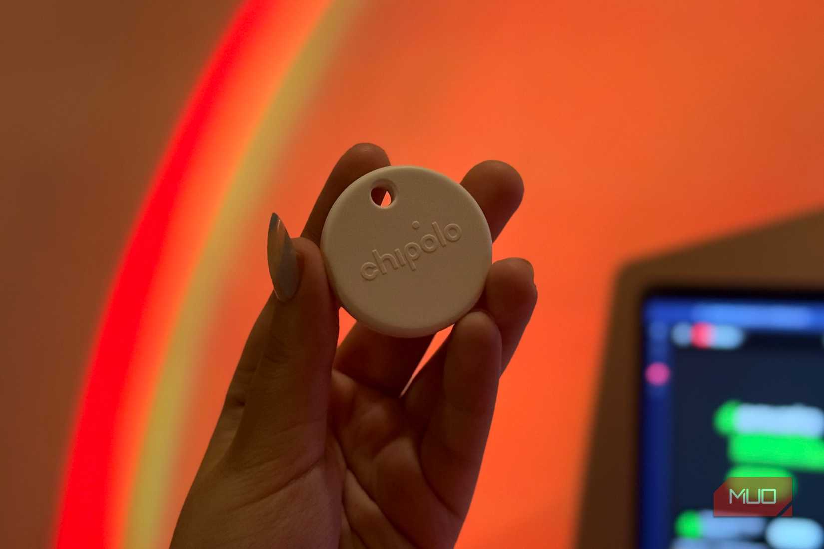 Chipolo tag held against warm rainbow-lit wall