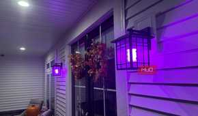 Porch wall lanterns glowing purple along the siding at night