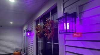 Porch wall lanterns glowing purple along the siding at night