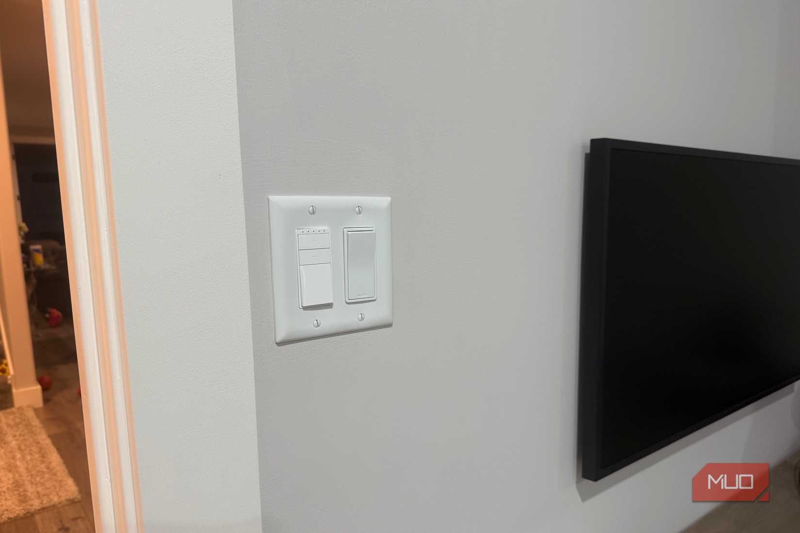 Smart dimmer beside paddle switch near wall-mounted TV