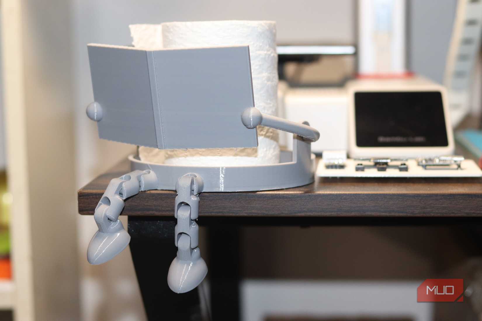 Toilet paper holder reading a book in front of 3D printer.