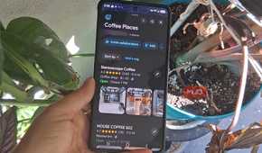 A hand holding a smartphone showing a Google Maps Coffee Places list beside several potted plants