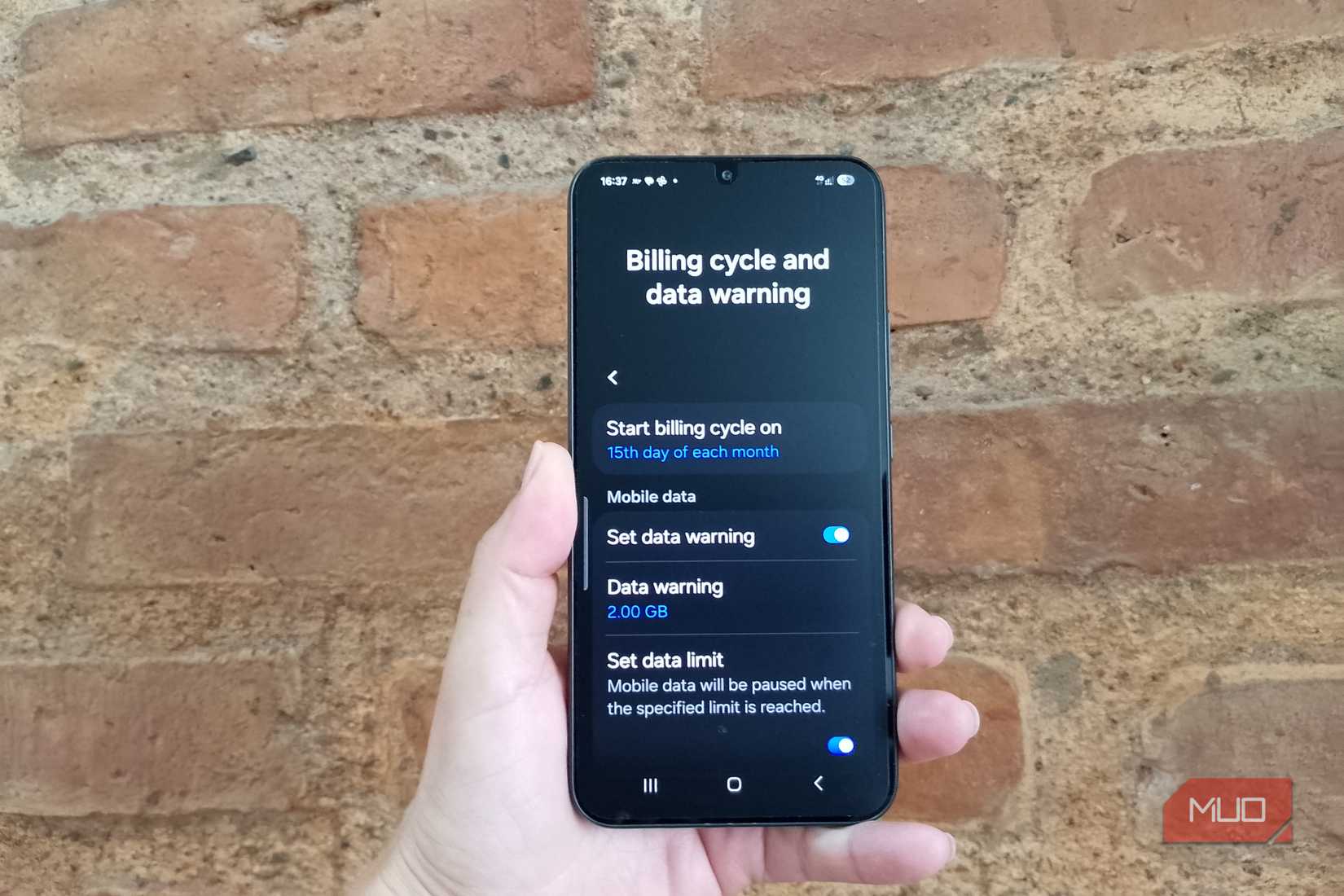 Hand holding a Samsung Galaxy phone showing a 2GB data warning, an enabled data limit, and a billing cycle starting on the 15th