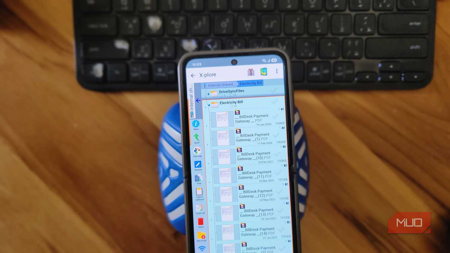 phone file manager showing electricity bill billdesk payment pdfs on wooden desk